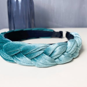 May include: A braided headband made of light blue velvet. The headband is a soft, flexible material and has a dark blue elastic band on the inside.