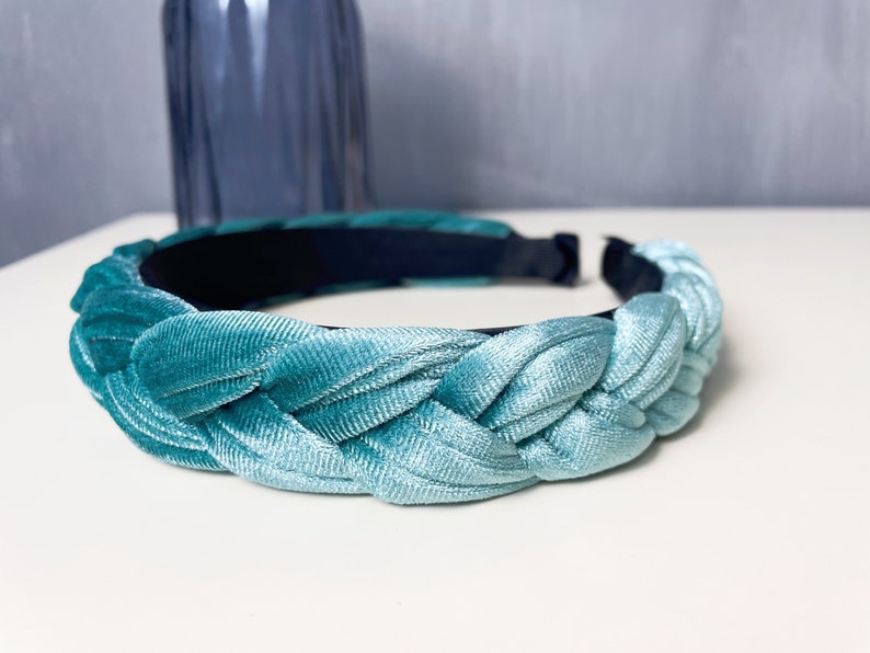 May include: A braided headband made of light blue velvet. The headband is a soft, flexible material and has a dark blue elastic band on the inside.
