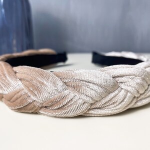 May include: A braided headband made of a soft, light beige velvet fabric. The headband is designed to be worn around the head and has a simple, elegant style.