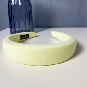 May include: A pale yellow headband with a black "HAND MADE" label. The headband is made of a soft, plush fabric.