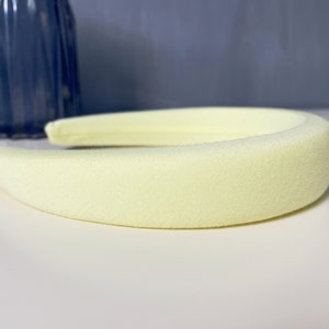 May include: A pale yellow headband made of soft fabric. The headband is thick and has a smooth, slightly textured surface.