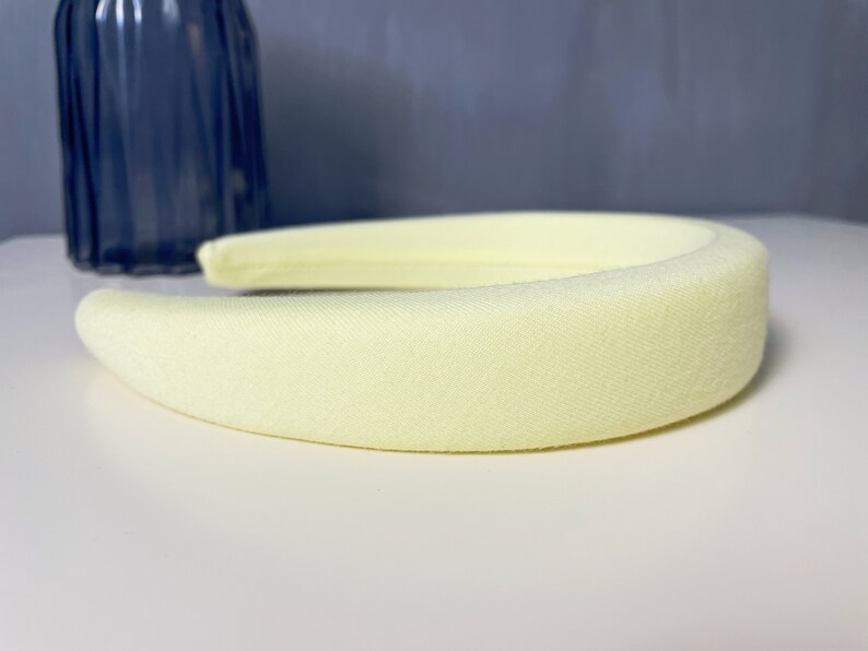 May include: A pale yellow headband made of soft fabric. The headband is thick and has a smooth, slightly textured surface.