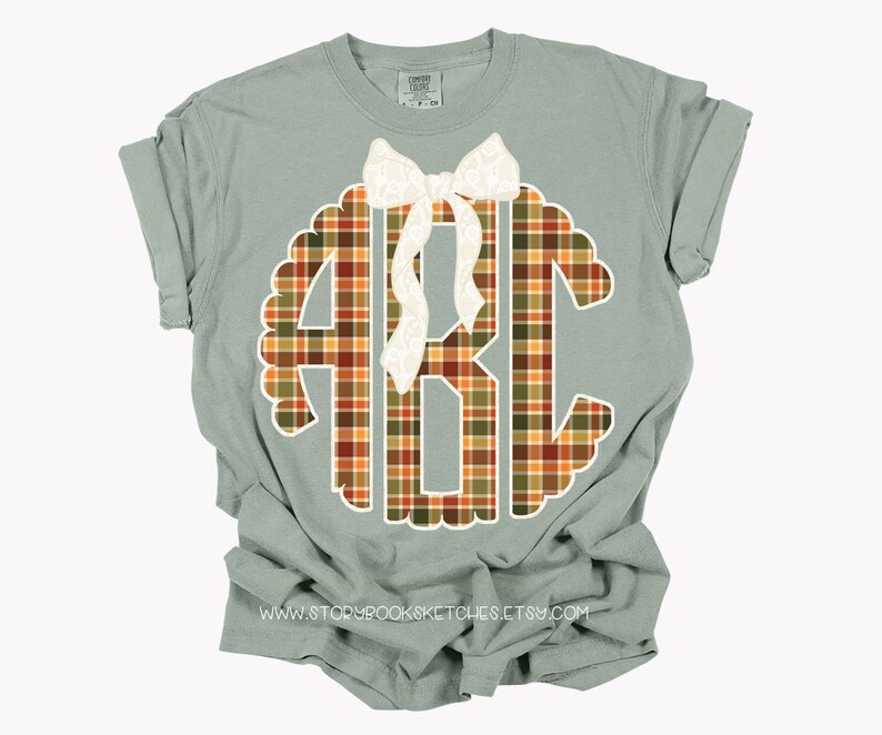 Puede incluir: Camiseta verde salvia con un monograma ABC a cuadros en naranja, marr&oacute;n y verde. Un lazo blanco adorna la parte superior del monograma. La camiseta tiene las mangas dobladas. Se ve el sitio web www.storybooksketches.etsy.com.
