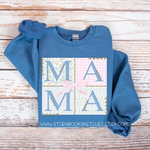 May include: A blue sweatshirt with a patchwork design that spells out "MAMA" in pink and blue floral patterns. The sweatshirt has a crew neck and long sleeves.