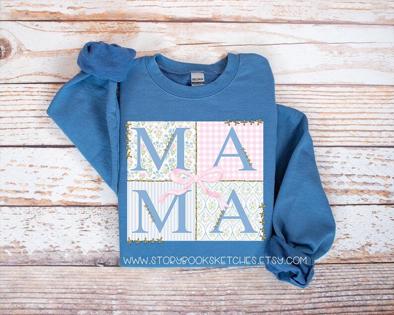 May include: A blue sweatshirt with a patchwork design that spells out "MAMA" in pink and blue floral patterns. The sweatshirt has a crew neck and long sleeves.