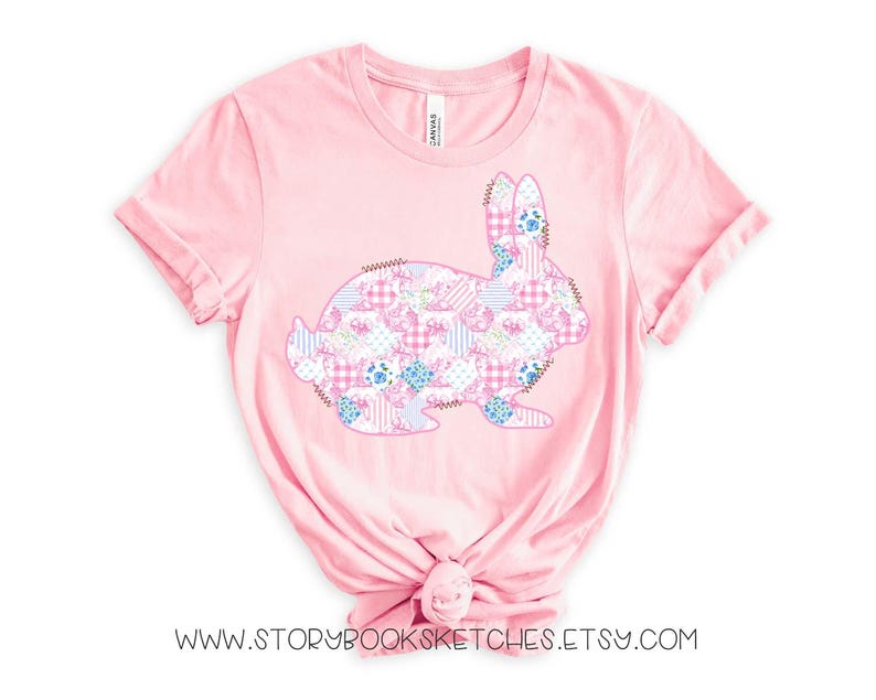 Pu&ograve; includere: Una maglietta rosa chiaro con un design a coniglio patchwork. Il coniglio &egrave; composto da vari motivi floreali e a quadri in rosa, blu e bianco. Il testo "WWW.STORYBOOKSKETCHES.ETSY.COM" &egrave; in basso.