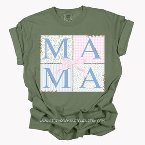 May include: A green t-shirt with a patchwork design featuring the word "MAMA" in blue letters with a pink bow. The design is surrounded by a gold glitter outline.