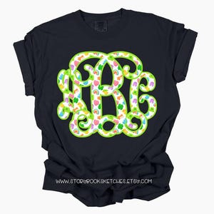 May include: A navy blue t-shirt featuring a large monogram design in the letters R, B, and C. The monogram is outlined in bright green and filled with a pattern of rainbows, hearts, and shamrocks. The website address www.storybooksketches.etsy.com is printed at the bottom.