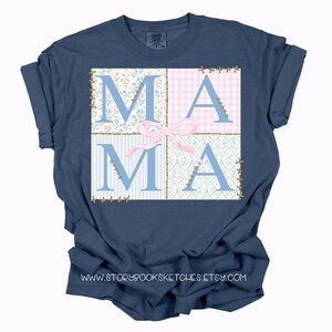 May include: A navy blue t-shirt with a patchwork design featuring the word "MAMA" in blue letters with a pink bow. The design is reminiscent of a quilt.