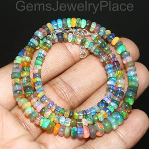 May include: A multi-strand necklace composed of small, colorful opal beads. The beads display a range of colors including green, blue, orange, and pink. The necklace is held in a hand, and the clasp is silver.