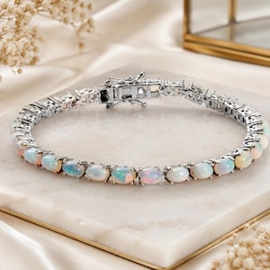 May include: A silver bracelet featuring a series of oval-shaped opals. The opals display a range of colors, including white, pink, and blue. The bracelet is secured with a clasp.
