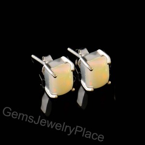 Op de afbeelding: Een paar vierkante opaal oorknopjes met een zilveren zetting. De opalen hebben een crèmewitte en gele kleur. De oorbellen worden gepresenteerd tegen een zwarte achtergrond. De tekst "GemsJewelryPlace" is zichtbaar.