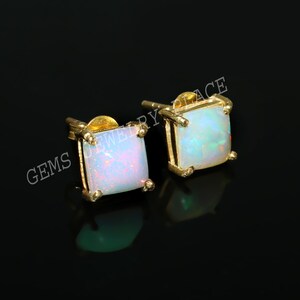 Peut inclure: Une paire de boucles d'oreilles clous carrées en or avec des pierres précieuses en opale blanche. Les boucles d'oreilles sont serties dans un design simple et élégant.