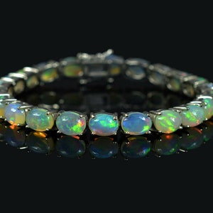 May include: A silver bracelet with a row of oval-shaped opals. The opals are a mix of white, green, and orange.