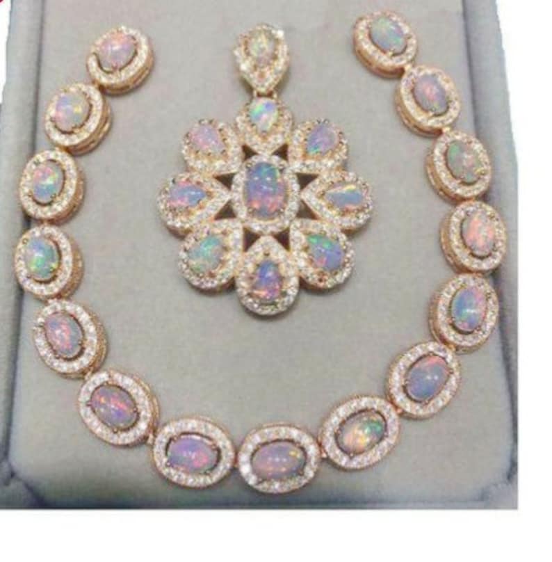 May include: A jewelry set featuring a necklace, earrings, and a pendant. The set has a gold-colored metal setting with oval-shaped opal stones and small clear stones. The pendant is flower-shaped, and the earrings are round.