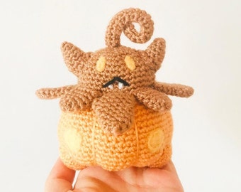 May include: A crocheted pumpkin-shaped plush toy with a brown, curled stem and a brown face with yellow eyes. The pumpkin is orange and has a crocheted pattern.
