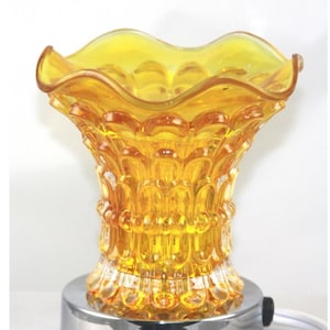 May include: A yellow glass oil diffuser with a decorative design and a chrome base. The diffuser has a wavy top and a cord for plugging in.