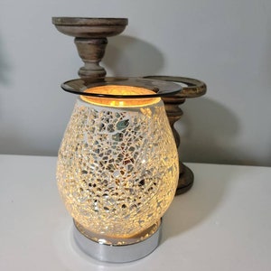 May include: A white and silver mosaic glass oil diffuser with a chrome base. The diffuser is lit and glowing.