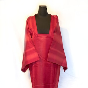 Puede incluir: Un kimono rojo oscuro con un escote cuadrado y un cierre de botón único. El kimono tiene un sutil patrón de diseños florales.