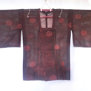 May include: A dark brown kimono with red circular patterns. The kimono has long sleeves and a square neckline. It is hanging on a hanger against a white background. The fabric appears to be a sheer, textured material.