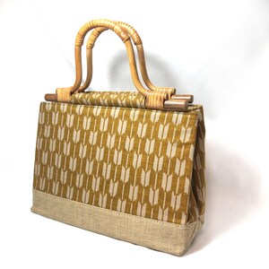 Peut inclure: Un sac fourre-tout en tissu brun et beige avec une poignée en bambou. Le sac a un motif géométrique de flèches blanches sur un fond brun.