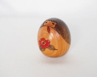 Miniature wooden kokeshi doll with a camellia flower