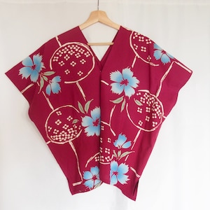 Peut inclure: Un haut de style kimono bordeaux avec un col en V et des manches courtes, orné d'un motif répété de fleurs bleu clair et de motifs circulaires blancs. Le vêtement est suspendu à un cintre en bois sur fond blanc.