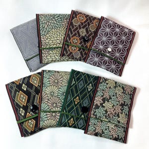 Puede incluir: Una colección de fundas de tela con varios diseños, incluyendo florales, geométricos y de hojas. Las fundas son en tonos grises, negros, marrones, verdes y rosas, con cierres elásticos verdes y ribetes decorativos.