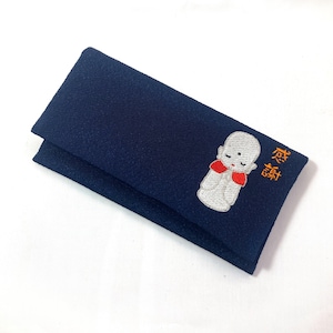 Könnte beinhalten: Ein marineblaues Stoffobjekt, möglicherweise eine Geldbörse oder ein Etui, mit einem gestickten Design. Das Design zeigt eine kleine, weiße Figur mit rotem Kragen und die japanischen Schriftzeichen für "Danke". Der Artikel ist gefaltet.