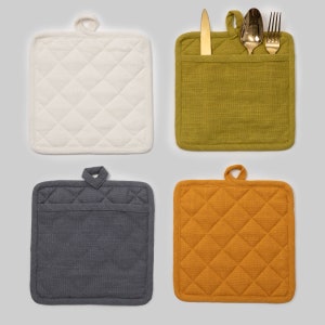 May include: Four quilted pot holders in different colours: white, green, grey, and orange. The green pot holder has a pocket for utensils, with a silver knife and two silver spoons inside.
