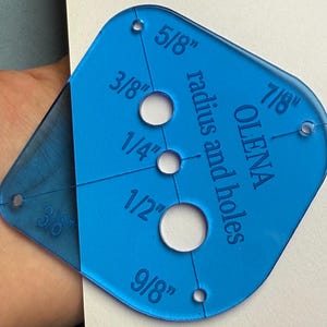 May include: A blue plastic template with holes of different sizes, labeled with their radius in inches. The template is labeled "OLENA radius and holes".