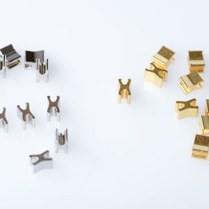 May include: Two groups of small metal connectors, one group is silver and the other is gold. The connectors are shaped like the letter 'X' and have a small loop on each side.
