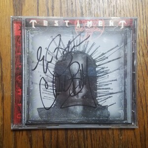 May include: A CD case with a black and white image of a person with a crown of nails. The case is signed by the band Testament. The band's name is printed in red on the top of the case.