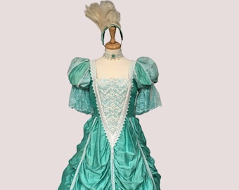 May include: A teal ball gown with white lace trim and puffed sleeves. The gown is on a mannequin with a white feather headpiece.
