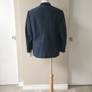 May include: A dark blue blazer on a wooden mannequin stand. The blazer has a classic style and is made of a smooth fabric.