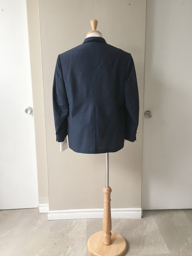May include: A dark blue blazer on a wooden mannequin stand. The blazer has a classic style and is made of a smooth fabric.