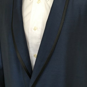 May include: A dark blue tuxedo jacket with a black satin lapel. The jacket has a single button closure and a white dress shirt underneath.