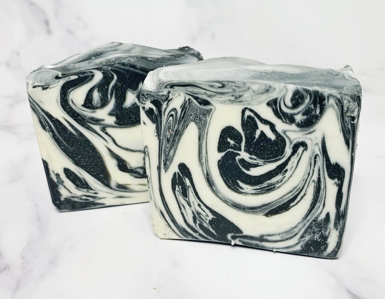May include: Two bars of handmade soap with a black and white marbled design. The soap is made with natural ingredients and is perfect for all skin types.