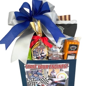 May include: A blue and silver gift basket with a blue ribbon and the words "Start Your Engines!" on the front. The basket is filled with various snacks and treats, including a bag of coffee, a block of cheese, and a bag of chocolate.