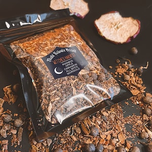 May include: A clear plastic bag filled with a blend of loose leaf tea. The tea is a mix of brown, orange, and black pieces. The bag has a label that reads "Night Rituals Recull Witches Harvest Rooibos Apple Cinnamon All Spice Marigold".