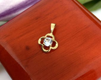 Pode incluir: Um pingente de ouro com uma pedra redonda transparente no centro, rodeado por um design de trevo de quatro folhas.