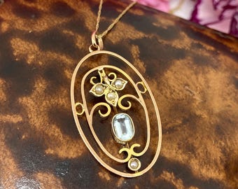 May include: A gold pendant necklace with a delicate oval frame featuring a light blue gemstone and pearl accents. The pendant is on a gold chain.