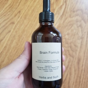 May include: A brown glass bottle with a dropper top and a label that reads "Brain Formula". The label also lists ingredients including blue vervain, gotu kola, blessed thistle, gingko, cayenne, ginger, rosemary, lobelia, and vodka. The label also includes the text "Herbs and Such".