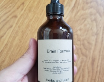 May include: A brown glass bottle with a dropper top and a label that reads "Brain Formula". The label also lists ingredients including blue vervain, gotu kola, blessed thistle, gingko, cayenne, ginger, rosemary, lobelia, and vodka. The label also includes the text "Herbs and Such".