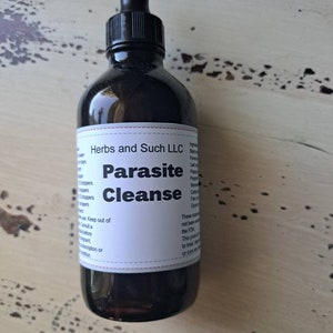 May include: A dark brown glass bottle with a dropper top. The label reads "Herbs and Such LLC Parasite Cleanse".