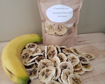 May include: A bag of dehydrated banana chips with a label that reads "Herbs and Such Dehydrated Banana Chips 100% Natural". A banana and a pile of banana chips are in the foreground.