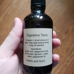May include: A dark brown glass bottle with a dropper top, labeled "Digestive Tonic". The label includes instructions for use and a list of ingredients: ginger root, peppermint leaf, fennel seed, glycerin, vodka, water, and peppermint oil. The label also includes the text "Herbs and Such".