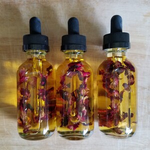 Puede incluir: Tres botellas de vidrio con goteros negros llenos de un l&iacute;quido amarillo y p&eacute;talos de rosa secos.