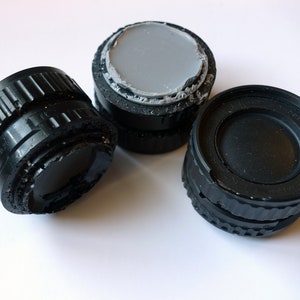 Peut inclure: Trois bouchons d'objectif d'appareil photo noirs, dont un avec un insert en caoutchouc gris.