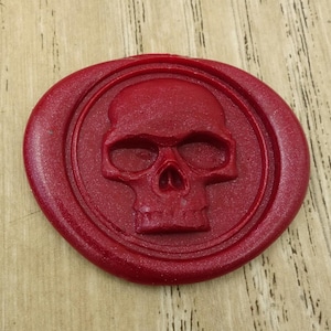 May include: A red wax seal with a raised skull design. The skull is detailed with eye sockets, a nose, and a mouth.